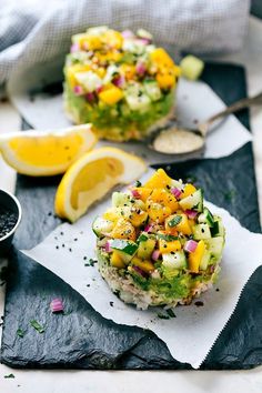 two bowls filled with food sitting on top of a table next to lemon wedges