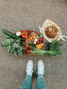 a person standing next to a basket full of vegetables on the ground with their feet propped up