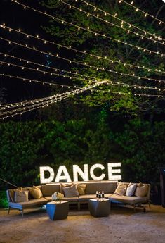 the dance sign is lit up at night with string lights strung above it and couches