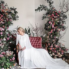 a woman is sitting on a couch surrounded by flowers