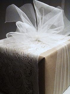 a gift wrapped in white lace and with a bow on the top is sitting on a table