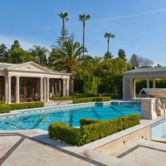 an outdoor swimming pool surrounded by greenery and palm trees, with fountain in the middle