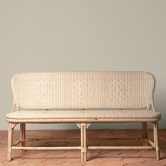 a wicker bench sitting on top of a wooden floor next to a gray wall