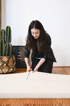 a woman cutting paper with a pair of scissors on the floor next to cacti