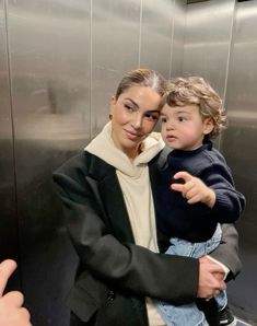 a woman holding a small child in her arms while standing next to an elevator door