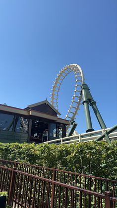 a roller coaster in front of a building with trees and bushes around it on a sunny day