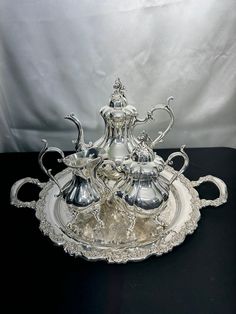 an ornate silver tea set on a black table