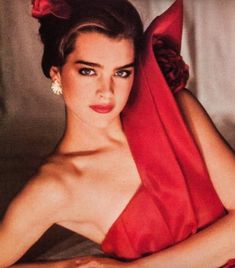 a woman in a red dress laying on a bed with her arms folded over her head