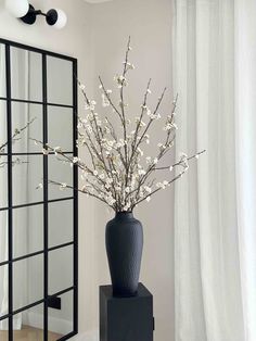 a black vase with white flowers in it sitting on a table next to a mirror