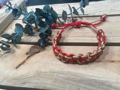 a red string bracelet sitting on top of a wooden table next to some green leaves