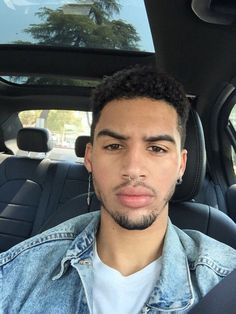 a man sitting in the back seat of a car wearing a jean jacket and earrings