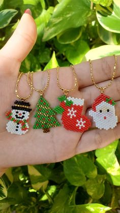 four christmas ornaments in the palm of someone's hand with green leaves behind them