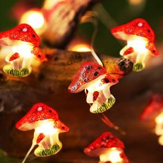 some red mushrooms are lit up on a tree branch with lights in the shape of ladybugs