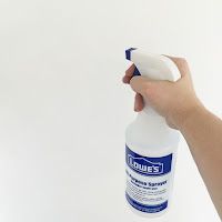 a hand holding a bottle of deodorant on top of a white wall