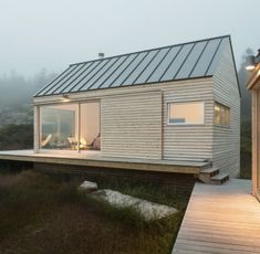 a small wooden house on the edge of a grassy field with a deck leading to it