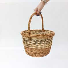 a woman's hand holding a wicker basket with handles and two sides, on a white background