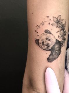 a small panda bear tattoo on the right inner arm and wrist, with flowers around it