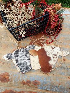 three cow hide ornaments sitting on the ground next to some pine cones and other christmas decorations