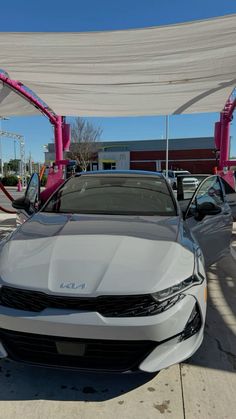 a car is parked under a canopy in front of other cars at a dealership