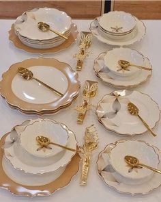 a table topped with lots of white plates and gold utensils on top of each other