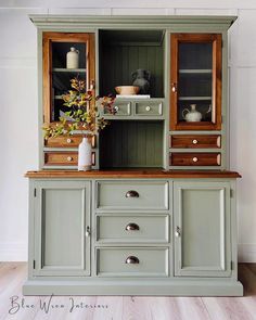 an old china cabinet is painted green with wood trimmings and flowers in the vase