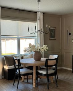 a dining room table with four chairs and a vase on the table in front of two windows