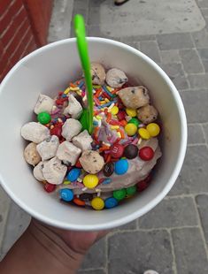 a person holding a cup filled with candy and candies on the sidewalk next to a brick wall