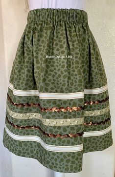 Traditional ribbon skirt in green on green leopard print with elevated details in beige/ivory striped, green floral crossgrain ribbon and brown sequin ribbon lovingly made by hand. A paper bag waist hugs the body, while also being comfortable to wear. See our sizing details below to find your perfect size.  Ready to ship! A long time symbol femininity, sisterhood and solidarity, used in ceremony and everyday, every skirt tells a story written by the woman who wears it. Perfect for every season, dressed up or down. Cross grain and sequin ribbons adorn our skirts and are chosen and arranged by hand during the design process. Each skirt is one of a kind, and may be the only skirt available in the indicated size, fabric, and ribbon combination. Right place, right time? We recommend buying the Ribbon Skirts Native American For Sale, Ribbon Skirts Native American Shirt, Ribbon Skirts Native American Top, Native Print Skirts, Ribbon Skirts Outfit, Ribbon Skirts Native American, Time Symbol, Ribbon Clothes, Skirt Traditional