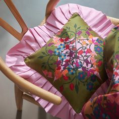 a pink and green pillow sitting on top of a wooden chair next to a cushion