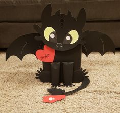 a paper cut out of a black dragon holding a red heart with the word love written on it