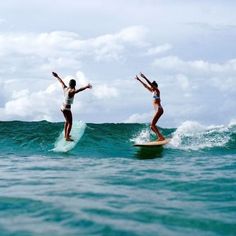 two women on surfboards in the ocean with their arms up and one standing on her board