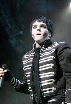 a male in a black and white striped jacket holding a microphone with his right hand