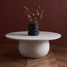 a white table topped with a black vase filled with flowers on top of a wooden floor