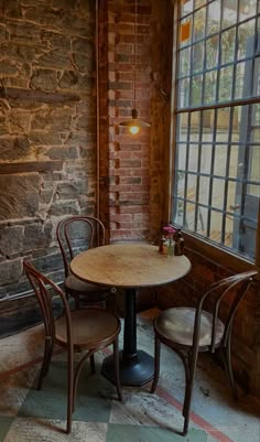 two chairs and a table in front of a window with a brick wall behind it