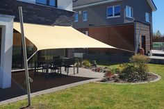 an outdoor patio area with a table and chairs under a large shade sail in front of a house