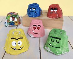 five different colored pots with faces painted on them sitting on a wooden table next to a block of wood