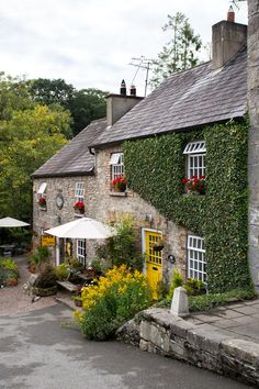 an old stone house covered in ivy with flowers and plants growing on the outside wall