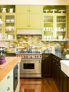 a kitchen with wooden floors and green cabinets, white dishes on the shelf above the stove