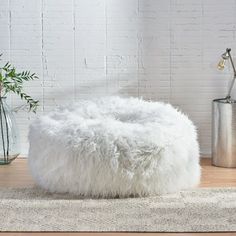 a white ottoman sitting on top of a wooden floor next to a potted plant