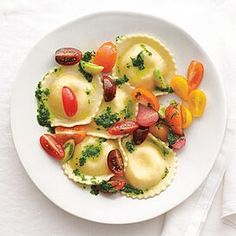 a white plate topped with ravioli covered in veggies and sauce next to a fork