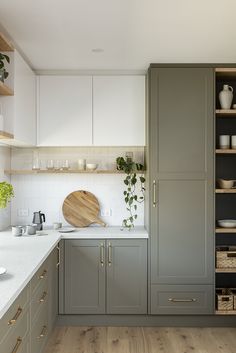 a kitchen with gray cabinets and white counter tops, wooden cutting board on the island