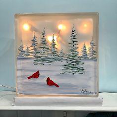 a red bird sitting on top of a glass block with lights in the trees behind it