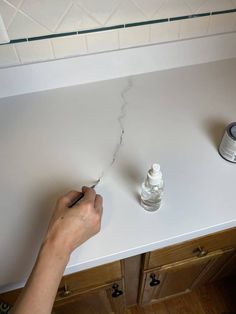 a person writing on a white counter top next to a can of paint and an empty bottle