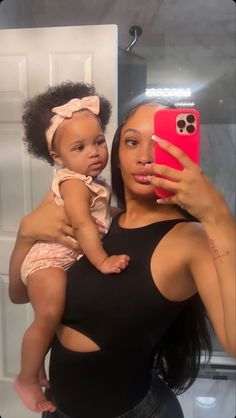 a woman holding a baby taking a selfie in front of a mirror with her cell phone