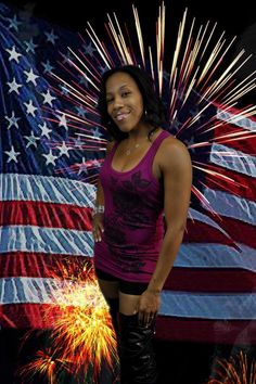 a woman standing in front of an american flag with fireworks on the ground behind her