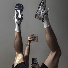 a man with his legs up holding a cell phone and wearing nike shoes while sitting on the floor