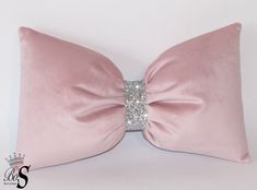 a pink pillow with a large bow on it's side and a diamond brooch in the middle