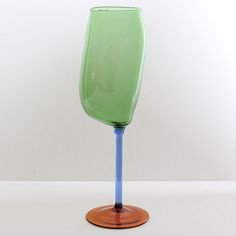 a green wine glass sitting on top of a wooden table next to a white wall