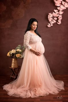 a pregnant woman in a pink gown standing next to a vase with flowers on it