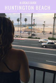 a woman is looking out the window at cars on the street and palm trees in front of her